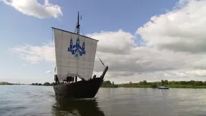Foto van een ouderwets zeilschip met één zeil, verder van hout, op grote waterplas.