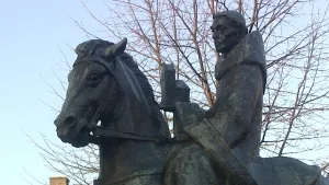 Foto van een beeld met Willibrord op een paard met boom op de achtergrond.