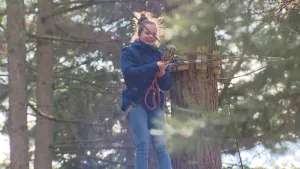 Foto van meisje in tuigje en aangelijnd aan een touw in een boomklimparcours, in het bos.