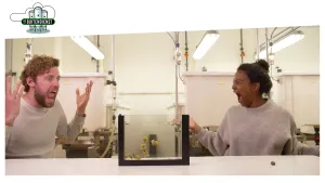 Foto van man en vrouw in laboratorium zitten aan een tafel bij een glazen kooi met kleine diertjes erin.