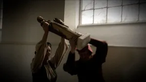 Foto van interieur van een kerk met groot raam en twee personen die samen een beeld dragen.