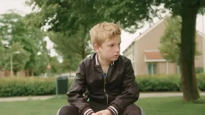 Foto van een jongetje dat buiten in het plantsoen zit.