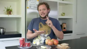 Foto van presentator in keuken die aantal voedingsproducten laat zien zoals appels, ei, blikje frisdrank.