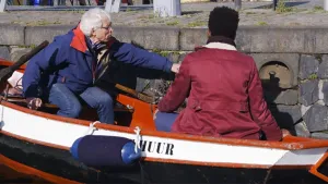 Foto van een klein motorbootje langs de kade van een gracht met erin twee mannen.