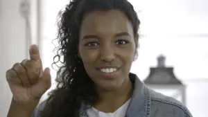 Foto van presentator, je ziet alleen haar hoofd, die met één hand een gebaar laat zien.