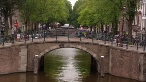 Foto van een brug te Amsterdam over de gracht heen, bomen erlangs, in de verte zie je volgende brug.