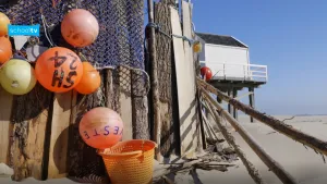Foto van vondsten vanaf het strand, strandjutten, die hangen aan een muur, zoals boeien, netten, plastic mand; op het strand.