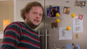 Foto van presentator bij een koelkastdeur met briefjes/kaarten met smiley-magneetjes eraan bevestigd.