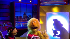 Foto van scène uit de Boterhamshow met Opperdepop en twee figuren in de studio aan tafel, van het ene figuur alleen het silhouette, politieagent.