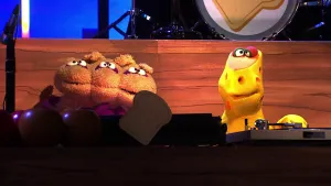 Foto van scène uit de Boterhamshow met in de studio aan de desk vier figuren (poppen), met pick-up en keyboard.