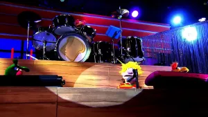 Foto van scène uit de Boterhamshow met André Hadé (pop) die zingt voor microfoon aan tafel, je ziet de studio met drumstel erachter.