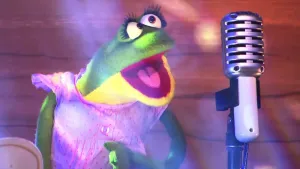 Foto van scène uit de Boterhamshow met kikker (pop) die zingt voor microfoon.