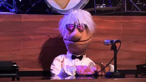 Foto van scène uit de Boterhamshow met Tiel Toetsemans (pop) aan de desk met microfoon.