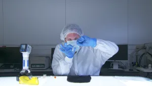 Foto van een man in beschermende werkkleding met mondkapje op die onderzoek doet naar DNA.
