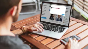 Foto van een man aan tafel achter een notebook/laptop en een smartphone/mobiele telefoon.