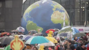 Foto van veel mensen rondom een grote nagemaakte wereldbol, velen hebben een paraplu op.