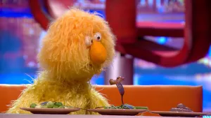 Foto van scène uit de Boterhamshow met Oma Dekker (pop) die aan tafel zit met twee borden met groentes erop.