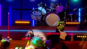 Foto van scène uit de Boterhamshow met de studio met drumstel op het podium en aantal figuren aan de desk (poppen).