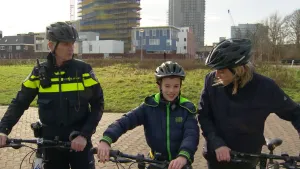 Foto van jongen en meisje op de fiets en politieagent op de fiets, staan stil op straat.