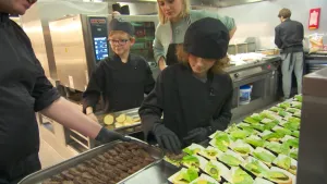Foto van een professionele keuken waarin kinderen en volwassenen aan het koken zijn.