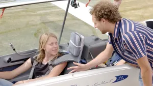 Foto van meisje dat zit in een zweefvliegtuig op de startbaan, de piloot staat erbij.