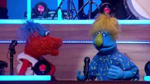 Foto van scène uit de Boterhamshow waarbij twee figuren, poppen, aan de desk die in gesprek met elkaar zijn.