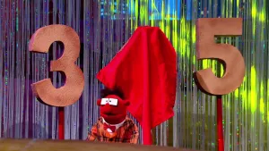 Foto van scène uit de Boterhamshow waarbij Pi R Kwadraat aan tafel zit bij een drie, een afgedekte vier, een vijf.