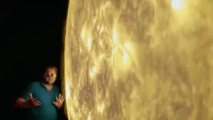Foto van een presentator bij een beeld van het oppervlak van de zon.