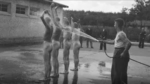 Foto, zwart/wit, ten tijde van Tweede Wereldoorlog waarop aantal mensen, bloot/naakt, staan die met waterslang worden afgespoten in Kamp Amesfoort.