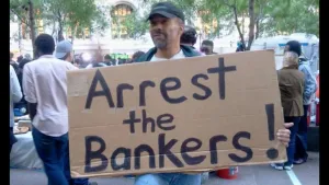 Foto van een man in een protestactie die een bord draagt met de tekst "Arrest the Bankers".