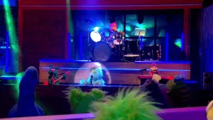 Foto van de Botehamshow waarbij je op het podium de band ziet en op de voorgrond drie figuren (poppen) die zitten aan de desk.