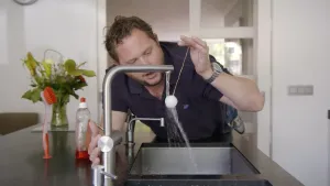 Foto van een man die bij een lopende kraan een proef doet met een bolletje aan een stokje.