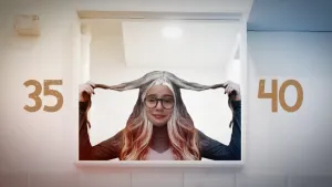 Foto van een vrouw achter een raam met bruin haar, maar bovenop haar hoofd grijs haar.