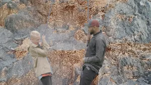 Foto van een man (bergbeklimmer) voor een rotswand geeft een jongetje aan touw instructies.