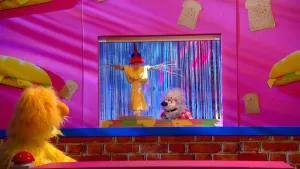 Foto van scène uit de Boterhamshow met Opperdepop aan de desk die kijkt naar toneeltje met een vogelverschrikker en Tineke (pop).