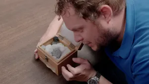 Foto van een presentator die op de grond ligt bij een doosje waarin een meteoriet.