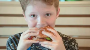 Foto van een jongetje (portret) dat een boordje hamburger eet.