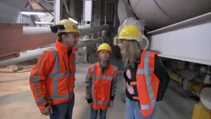 Foto van man en twee kinderen met helms op in fabriek met machines.