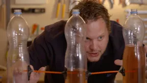 Foto van presentator in testruimte doet een proef met drie plastic drinkflessen.