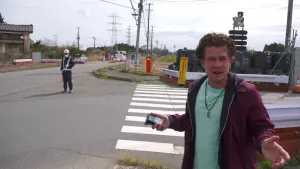 Foto van een presentator op straat nabij hoogspanningsmasten te Fukushima.