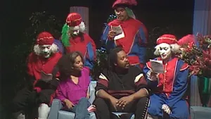 Foto van groep mensen, als Zwartepiet verkleed, maar zijn niet zwart, en man en vrouw zitten op een bank.