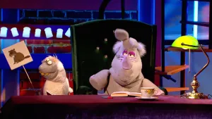 Foto van scène uit de Boterhamshow met Nico de Neushoorn, draagt tekening van een bever, en zijn assistent Stella aan tafel.