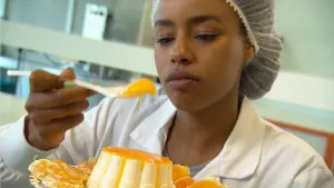 Foto van een vrouw in fabrieks-/laboratoriumkleding die een pudding proeft.