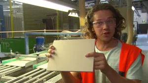 Foto van presentator die een tegel vasthoudt in een tegelfabriek.