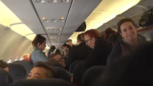 Foto van het interieur van een vliegtuig met veel passagiers die nog moeten gaan zitten, aantal zitten al.