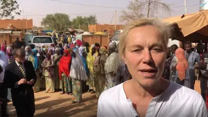 Foto met presentator met op de achtergrond beelden van een drukke straat met veel mensen in een ontwikkelingsland.
