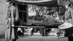 Zwart/wit-foto van de tijd van de Spaanse griep waarop twee personen met mondkapjes op een brancard met een afgedekt lijk dragen.