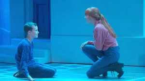 Jongetje zit samen met vrouw, Tess Milde, op het toneel dat blauw verlicht is.