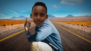 Foto van jongetje die zit op een lange rechte weg door woestijnachtig landschap met blauwe hemel erboven.