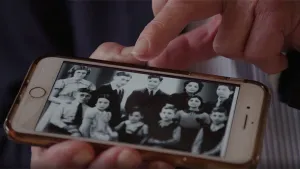 Foto van een hand die een mobiele telefoon vasthoudt waarop zwart-wit/foto staat van mensen ten tijde van de Tweede Wereldoorlog.